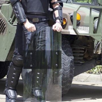 A man standing beside an army truck holding a RiotReady riot shield